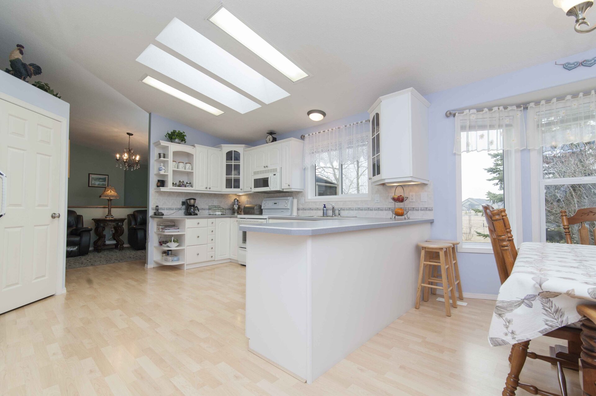Bright kitchen with white cabinets, a center island with two stools, wood flooring, skylights, and a dining area by large windows new construction plumber san francisco.